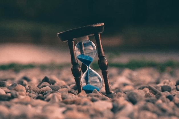 Egg timer with blue sand in it sat on pebbles